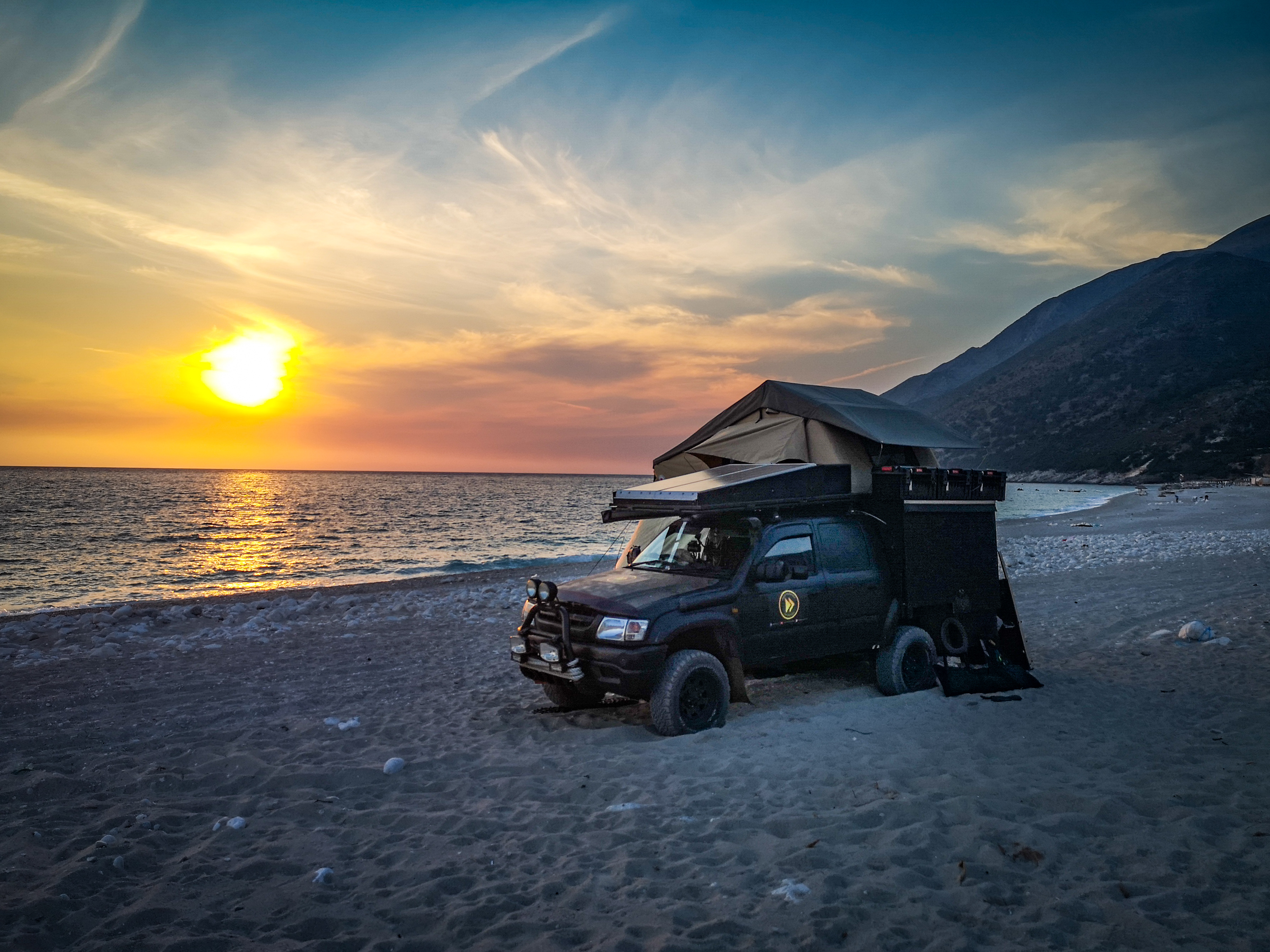 Zachód słońca, samochód terenowy na plaży w Albanii. Obozowanie, spanie  na dziko.
Sunset, 4x4 truck on a beach in Albania. Wild camping, sleeping, camping on a beach in Albania.